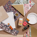 Crafting supplies including floral paper, Mod Podge, and a brush on a brown surface.